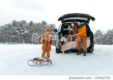 Winter portrait of a family sit on car trunk enjoy their vacation in forest Winter portrait of a family sit on car trunk enjoy their vacation in forest 87662702