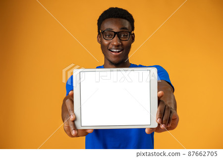 African american man showing blank digital tablet screen with copy space in yellow studio. African american man showing blank digital tablet screen with copy space in yellow studio. 87662705