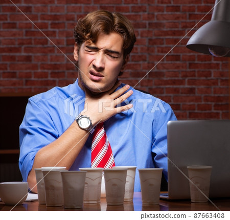 Young employee drinking coffee working at night shift 87663408