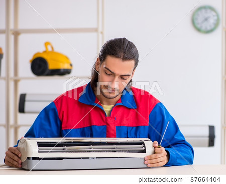 Young male contractor repairing air-conditioner at workshop Young male contractor repairing air-conditioner at workshop 87664404