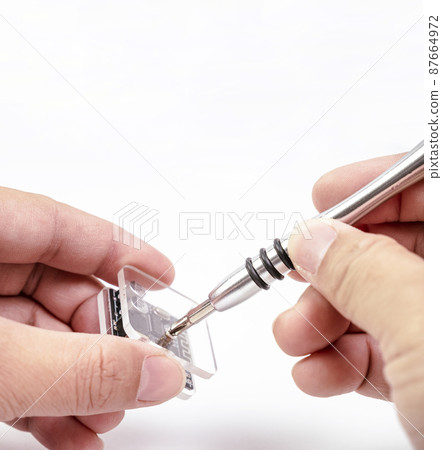 Electronic technician removing metal nut with a precision screwdriver for electronic repair 87664972