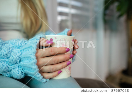 A woman's hands wrap around a mug of hot drink. 87667028