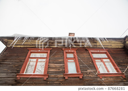 Frightening transparent icicles hang on the edge of the roof. Frightening transparent icicles hang on the edge of the roof. 87668281