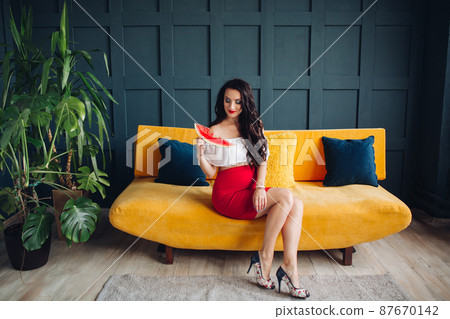Stylish pregnant woman sitting on orange sofa and Stylish pregnant woman sitting on orange sofa and 87670142