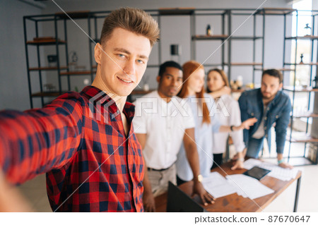 Successful team of young multi-ethnic startup businesspeople making selfie photo in coworking space and smiling looking at camera. Boss and cheerful subordinate officials making selfie in office. Successful team of young multi-ethnic startup businesspeople making selfie photo in coworking space and smiling looking at camera. Boss and cheerful subordinate officials making selfie in office. 87670647