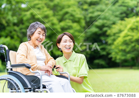 Seniors in outdoor wheelchairs and middle staff caring for them Seniors in outdoor wheelchairs and middle staff caring for them 87673088