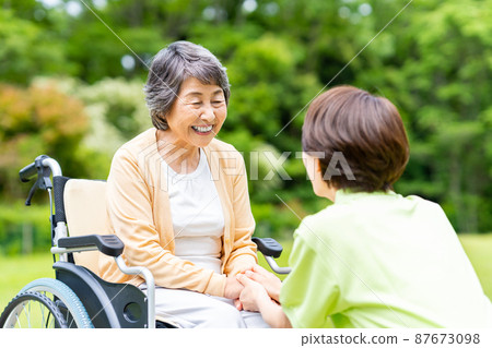 Seniors in outdoor wheelchairs and middle staff caring for them Seniors in outdoor wheelchairs and middle staff caring for them 87673098