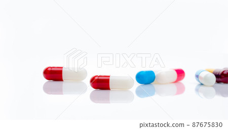 Red-white antibiotic capsule pill on blur multi-colored capsules background. Antibiotic drug resistance concept. Pharmacy horizontal banner. Prescription drugs. Pharmaceutical industry. Healthcare. Red-white antibiotic capsule pill on blur multi-colored capsules background. Antibiotic drug resistance concept. Pharmacy horizontal banner. Prescription drugs. Pharmaceutical industry. Healthcare. 87675830