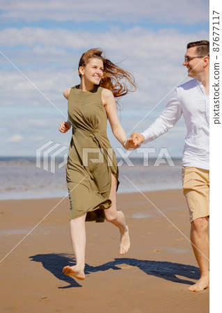 a couple of a man and a woman are walking on the beach or running along the sand along the seashore. beautiful and young a couple of a man and a woman are walking on the beach or running along the sand along the seashore. beautiful and young 87677117