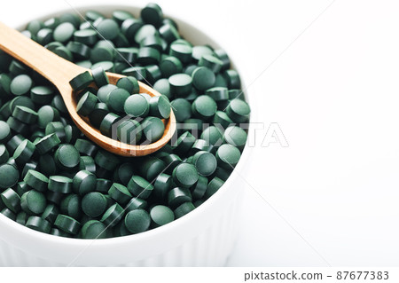 Organic spirulina tablets in a white cup with a wooden spoon Organic spirulina tablets in a white cup with a wooden spoon 87677383
