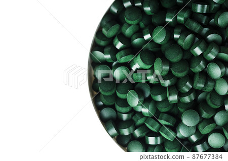 Green tablets made of natural organic spirulina in a cup on a white background with free space 87677384