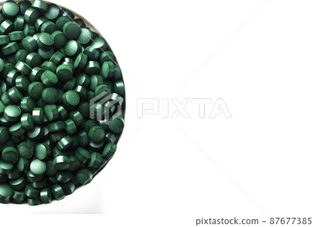 Green tablets made of natural organic spirulina in a cup on a white background with free space 87677385