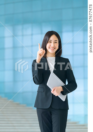 A business woman in a young suit standing with a bassocon at the entrance of the office 87677478