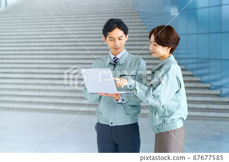 Male and female engineers in work clothes who consult while looking at a computer Male and female engineers in work clothes who consult while looking at a computer 87677585