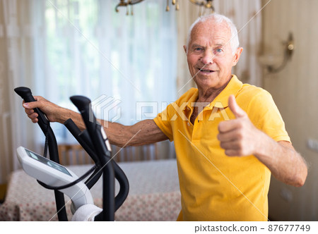 Mature man exercising on an elliptical machine and showing thumb up Mature man exercising on an elliptical machine and showing thumb up 87677749
