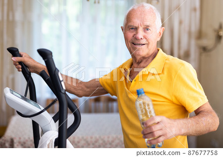 Man with bottle of water training with cross-trainer Man with bottle of water training with cross-trainer 87677758
