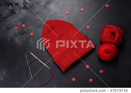 Red warm knitted women's hat on a concrete background 87679756