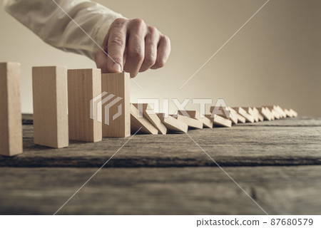 Businessman stopping collapsing wooden dominos 87680579