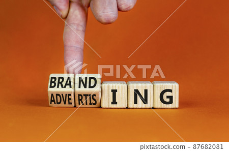 Branding and advertising symbol. Businessman turns wooden cubes and changes the word Advertising to Branding. Beautiful orange background, copy space. Business branding and advertising concept. 87682081