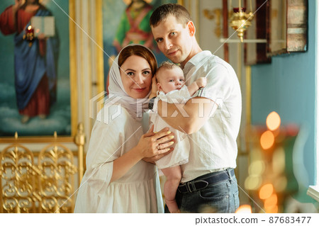 man and woman with baby son in light-colored robes by window in church. man and woman with baby son in light-colored robes by window in church. 87683477