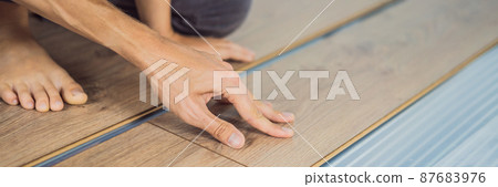 BANNER, LONG FORMAT Father and son installing new wooden laminate flooring on a warm film floor. Infrared floor heating system under laminate floor BANNER, LONG FORMAT Father and son installing new wooden laminate flooring on a warm film floor. Infrared floor heating system under laminate floor 87683976