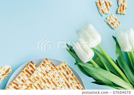 Happy Passover concept. Matzo and white tulips on a blue background. Religious Jewish holiday Pesach. Copy space, flat lay. Happy Passover concept. Matzo and white tulips on a blue background. Religious Jewish holiday Pesach. Copy space, flat lay. 87684078