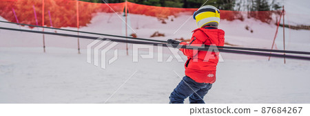BANNER, LONG FORMAT Boy uses a training lift. Child skiing in mountains. Active toddler kid with safety helmet, goggles and poles. Ski race for young children. Winter sport for family. Kids ski lesson 87684267