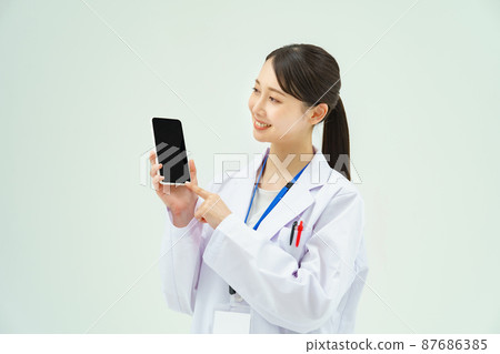 一個穿著白大褂的女人拿著智能手機 87686385