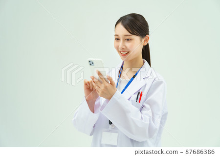 一個穿著白大褂的女人拿著智能手機 一個穿著白大褂的女人拿著智能手機 87686386