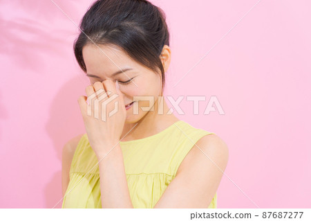 A woman holding her eyes pink background 87687277