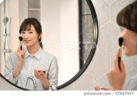 A woman putting on makeup in front of a mirror A woman putting on makeup in front of a mirror 87687447