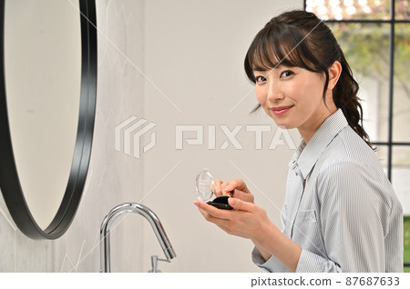 A woman putting on makeup in front of a mirror A woman putting on makeup in front of a mirror 87687633