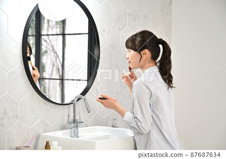 A woman putting on makeup in front of a mirror A woman putting on makeup in front of a mirror 87687634