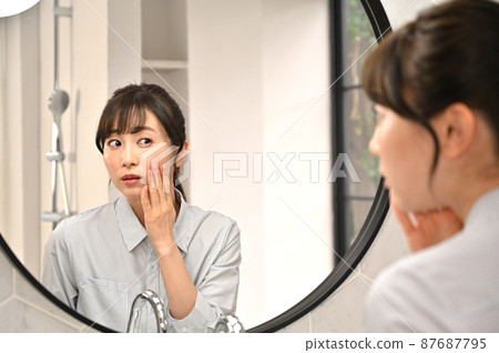 A woman checking her skin in front of a mirror 87687795