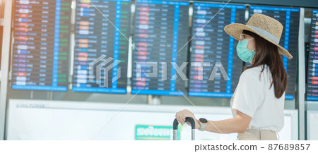 Young female wearing face mask with luggage walking in airport, protection Coronavirus disease infection, Asian woman traveler with hat. Time to travel, Test and Go and vaccine booster dose concept 87689857