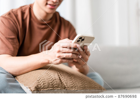 Technology Concept The man sitting next to a pot of plant, putting a small pillow on his lap, and checking something on his smartphone 87690698