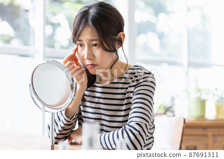 Middle-aged woman suffering from skin problems in front of the mirror 87691311