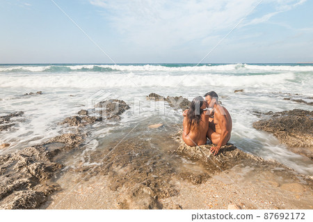 Couple of nudists kissing on beach near sea Couple of nudists kissing on beach near sea 87692172
