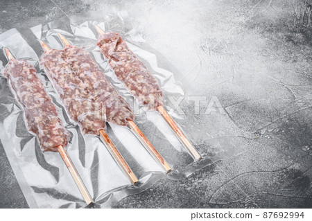 Vacuum packed raw meat skewers, on gray stone table background, with copy space for text 87692994