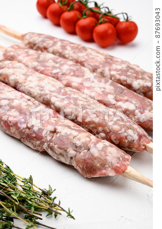Minced and shaped lamb mutton kebabs, with grill ingredients, on white stone table background Minced and shaped lamb mutton kebabs, with grill ingredients, on white stone table background 87693043