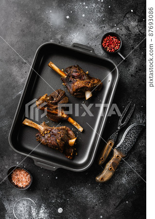 Slow Cooked Lamb Shanks meat, on black dark stone table background, top view flat lay Slow Cooked Lamb Shanks meat, on black dark stone table background, top view flat lay 87693086