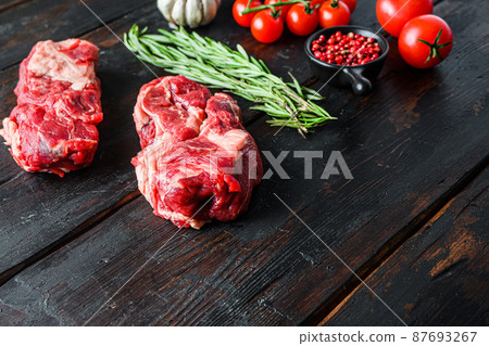 Organic raw chuck eye roll beef steak cut with rosemary red onin, garlic peppercorns and tomatoes on old dark wooden table. Side view with space for text. 87693267