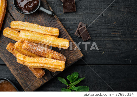 Churros with caramel Traditional Spanish cusine, on black wooden table background, top view flat lay with space for text, copyspace Churros with caramel Traditional Spanish cusine, on black wooden table background, top view flat lay with space for text, copyspace 87693334
