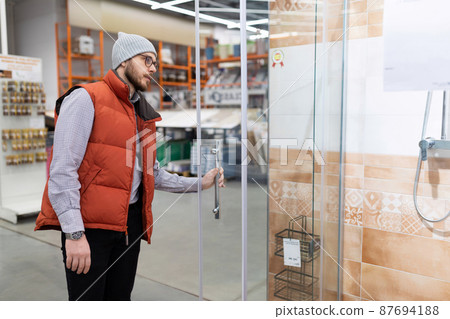 a man in a store examines a shower stall in the plumbing department 87694188