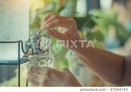 Hand of thirsty woman press the drinking cool water into a clear glass. Female finger pressing a button cold drinking water with cooler dispenser. Healthcare and Household Concept. Selective focus. Hand of thirsty woman press the drinking cool water into a clear glass. Female finger pressing a button cold drinking water with cooler dispenser. Healthcare and Household Concept. Selective focus. 87694743