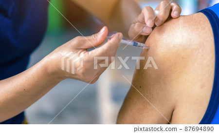 Close up to female doctor holding syringe making covid 19 vaccination injection dose in shoulder of senior man. Vaccinating elderly patient, healthcare concept. Covid-19 or coronavirus vaccine. 87694890
