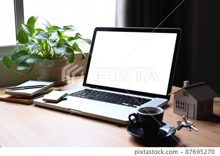 Mockup laptop computer, house model and keys on wooden table. Mortgage and real estate investment concept. Mockup laptop computer, house model and keys on wooden table. Mortgage and real estate investment concept. 87695270
