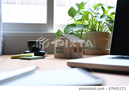 Small house model with laptop on wooden table. Mortgage and real estate investment concept. Small house model with laptop on wooden table. Mortgage and real estate investment concept. 87695271