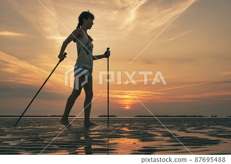 Girl practicing Nordic walking on the beach at dawn Girl practicing Nordic walking on the beach at dawn 87695488