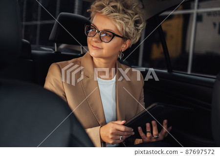Female Entrepreneur Looking Through Window While Sitting on Back Seat of a Luxury Car 87697572